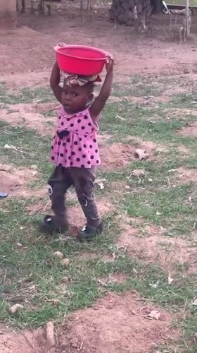 Toddler carries basin on head along dirt path in Akwanga