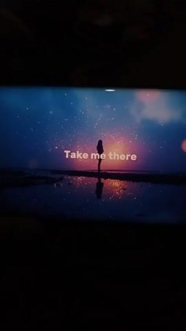 The video shows a TV screen playing a video with a girl standing near a body of water. Above her and reflected in the water are what appear to be stars in the night sky. The text "To the moment time stood still" appears on the screen, followed by "Where your heartbeat's all I feel."