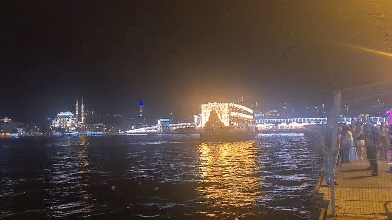 Illuminated boat crossing the Bosphorus past Istanbul's night skyline