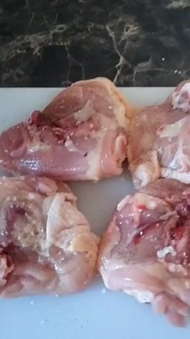 The video shows four raw chicken pieces on a white cutting board. The chicken appears to be skin-on and has some visible fat and a reddish hue. The background is blurred but suggests a dark, possibly granite countertop. The lighting appears to be artificial and bright, casting a slight glare on the chicken. There is no indication of time of day, weather, or specific location within Horenka. No people are visible, and no text is present in the video. The activity appears to be food preparation, specifically the raw presentation of chicken pieces. The overall tone is neutral and observational, focusing on the raw ingredients.