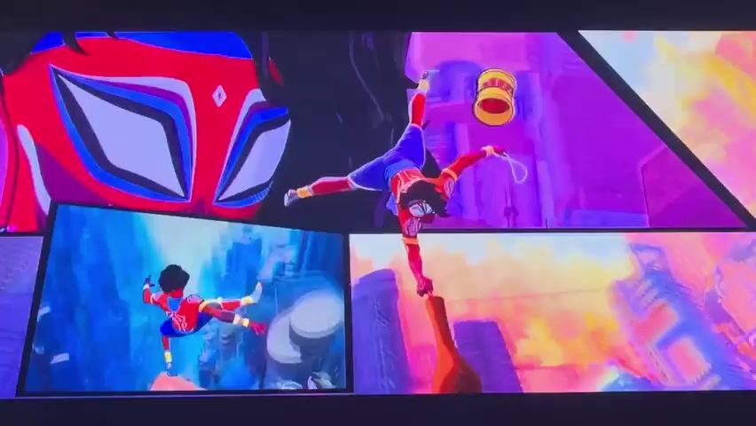 This media file showcases a vibrant, animated scene featuring multiple Spider-People in action. The primary subject is a young Black woman, Peni Parker, dressed in a red and blue suit with distinctive Spider-Man-like webbing patterns. She is shown in various dynamic poses, including a handstand on a stack of red spheres and leaping through the air. Objects like a yo-yo and what appears to be a wooden bat are also visible, held by Peni.

The scene is set against a surreal, stylized cityscape bathed in bright, almost neon colors, predominantly purples, pinks, and blues. The architecture is angular and futuristic, suggesting an urban environment but with a dreamlike or comic-book aesthetic. The time of day appears to be daytime, with a bright sky, though the intense colors contribute to a surreal atmosphere. There is no indication of specific weather conditions.

In addition to Peni Parker, other Spider-People are present. One appears to be Miles Morales in his classic Spider-Man suit, and another a female Spider-Woman in a white costume. They are seen interacting with Peni, forming a human pyramid on the stack of spheres, and in separate panels that seem to be integrated into the larger scene, showing Peni in different poses. The overall mood is energetic and action-packed, conveying a sense of heroic effort or a spectacular performance.

No visible text is present in the frames. The location context of Vozrozhdeniye, Russia, is not visually discernible from the imagery itself, which presents a more abstract and universal urban fantasy.