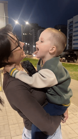 Woman holds child outside apartment building in Perm