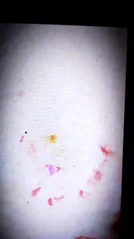 A video displays a young boy in a white t-shirt and purple shorts, lying on his back on a patterned rug. A red curtain hangs behind him, and the scene is framed by dark borders. The footage is grainy and has a vignetted effect.