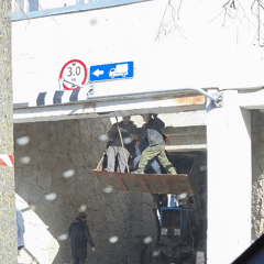 Three men stand on tractor bucket under low overpass