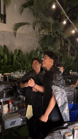 Bartenders pose with makeshift capes at outdoor bar in Kuta