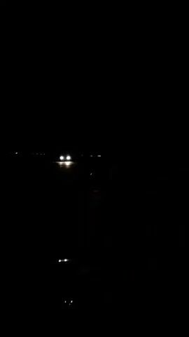 The video shows a dark, grainy scene.  There are faint lights visible in the distance. The camera appears to be still.