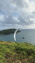 Paraglider over island waters, crowd watches from Rawai hilltop