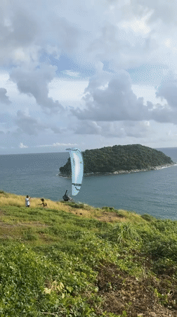 Paraglider over island waters, crowd watches from Rawai hilltop