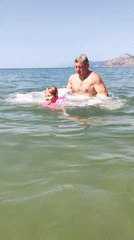 Busy pebble beach, swimming and playing in calm summer water