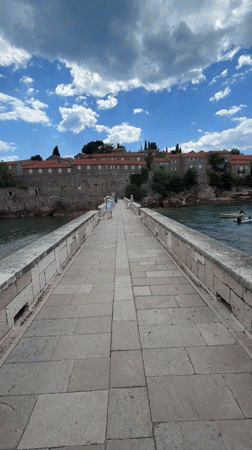 Couple walks stone bridge to Sveti Stefan island Montenegro