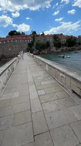 Couple walks stone bridge to Sveti Stefan island Montenegro