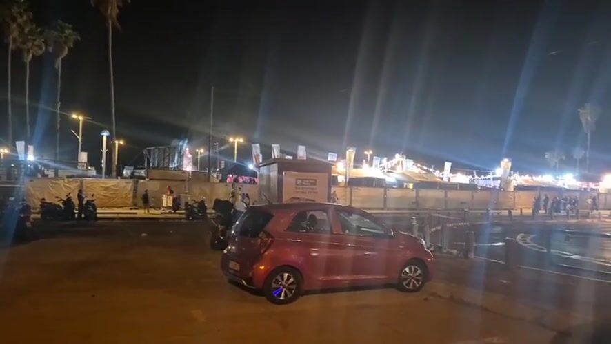 Red car parked on illuminated Tel Aviv promenade