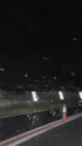 The video is shot from the inside of a moving vehicle at night. Raindrops are visible on the windshield. The roadside has several orange and white reflectors. The background is dark, obscuring the surrounding environment. A musical score plays throughout the video.