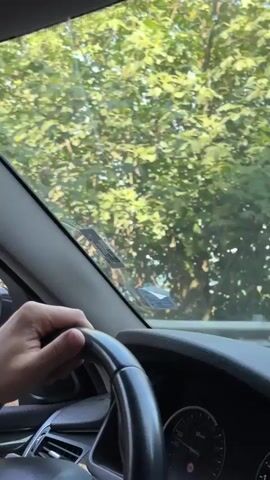 A first-person perspective video shows someone driving a car. The driver's hands are on the steering wheel. Through the windshield, trees and the ocean can be seen. The video shows the view from inside the car as it drives along a road, with glimpses of the sea and vegetation outside. The dashboard and interior of the car are also visible.