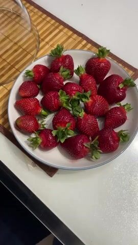 A hand picks up a strawberry from a plate of strawberries. The plate is on a placemat.