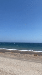 Morning on Santorini's black sand beach, sun and surf.