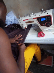 Person operates sewing machine with dark fabric at morning hour