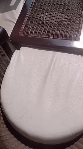 The video shows a balcony with a chair and a small table. The balcony overlooks a green valley with some buildings. The sun is shining brightly in the sky, which is partially covered with clouds. The camera pans up to show the view and then focuses on the sun.