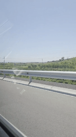 Vehicle travels paved road in Kosh, Armenia during sunny conditions