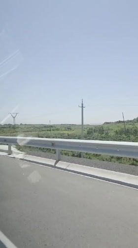 Vehicle travels paved road in Kosh, Armenia during sunny conditions
