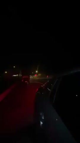 The video starts with a view from inside a car stopped on a street at night. Streetlights and the taillights of other vehicles are visible in the distance. The camera pans upward, revealing a dark sky with sparse lights, possibly from a distant city or buildings, along the horizon. The video then ends.