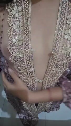 The video shows a close-up of a person wearing a sheer, ornate purple garment with gold lace detailing. The garment has a deep V-neckline, revealing the upper chest area. The person's hands are visible, adjusting the garment. The background is indistinct, appearing to be an indoor setting. The lighting is dim.