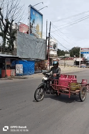 Motorcyclist transports gas tanks through Indonesian commercial district intersection
