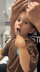 Toddler brushes teeth with adult help in Kiryat Bialik bathroom