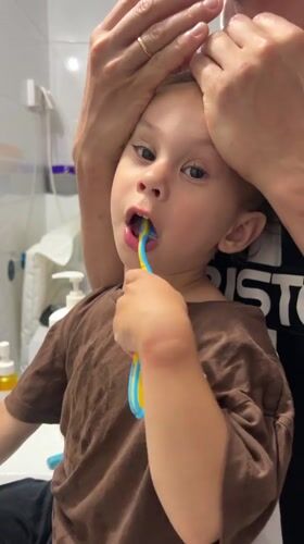 Toddler brushes teeth with adult help in Kiryat Bialik bathroom