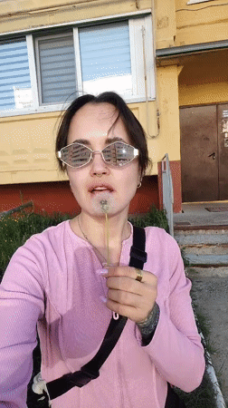 Woman holds dandelion outside yellow building in Noviy, Russia