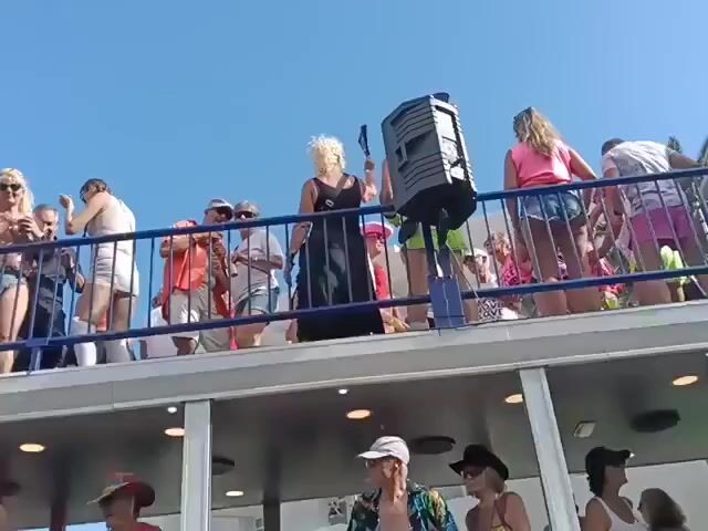 The video shows a double-decker bus, with people on both levels, in what appears to be a Pride celebration. The top level has people dancing and walking around, with a speaker in the middle. The lower level also has people, some of whom are wearing Pride-themed clothing. The bus is decorated with "Pride" banners and related imagery. The sky is clear and blue, suggesting a sunny day. The bus features logos for INFINITY SW CLUB.