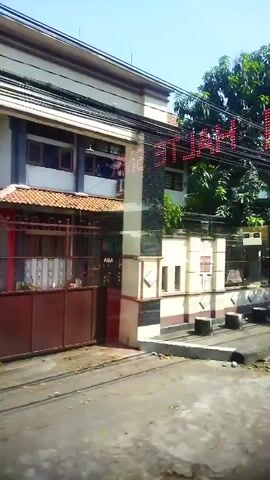 The video shows the exterior of a building with a large red metal gate. Above the gate, there is a sign with red LED lights that spells out "METRO". The building has a tiled roof and several windows. There are trees and power lines visible in the background. The overall scene appears to be a street in a residential or commercial area. The camera is positioned at a low angle, looking up at the building.