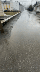 Person in black jacket walks wet city streets