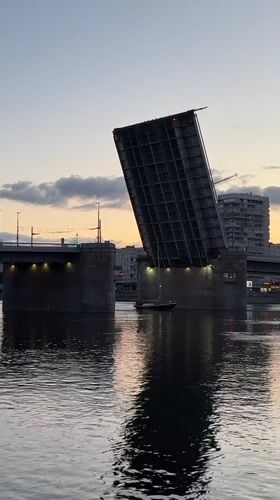 Sailboat passes raised drawbridge at sunset in Saint Petersburg