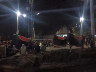 Nighttime ceremonial gathering with effigies and crowd in Gedongombo