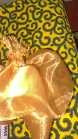 A hand holds a gold-colored, sheer fabric that lies on a yellow and black fabric. The hand moves the sheer fabric to show more of the yellow and black fabric underneath. The yellow and black fabric is decorated with a repeating swirling pattern. The sheer fabric appears to be crinkled.