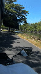 Motorcycle rider films road alongside canal in Denpasar