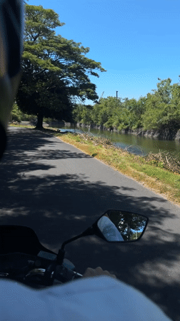Motorcycle rider films road alongside canal in Denpasar