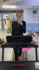 Woman exercises on treadmill while using smartphone in Russian gym
