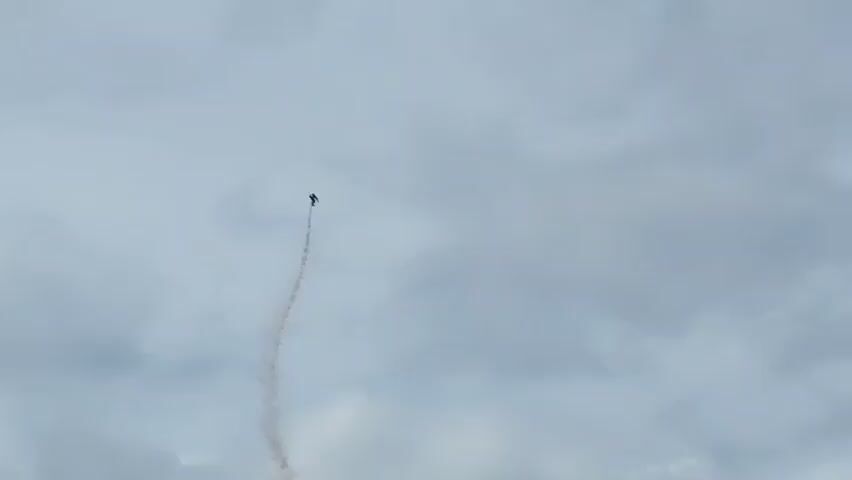 A person is skydiving against a cloudy sky, leaving a trail of smoke behind them.
