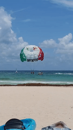 Parasailers display Mexican flag colors over Playa del Carmen waters