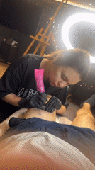 Tattoo artist works on client's leg during session