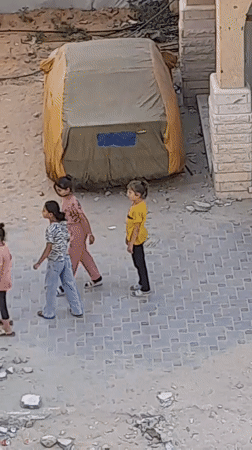 Children on a paved area near a large tent in Khan Yunis