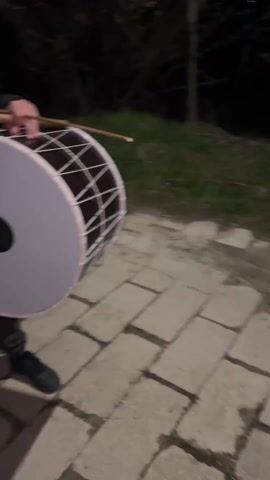 The video shows a group of people holding up a large white banner at night. The banner is inscribed with Cyrillic lettering. The scene is dimly lit. The people are standing on a paved area. There is a dog barking in the background.