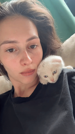 Woman holds white kitten, electronic device in Yekaterinburg home