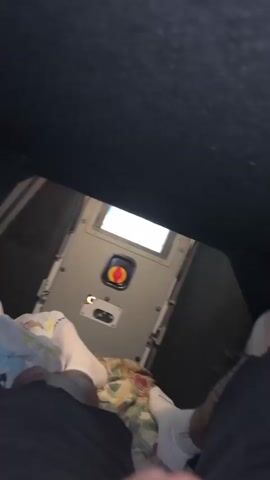 The video shows a view from inside a confined space. There's a person lying down, wearing white socks and black pants, and covered with a floral blanket. The view is angled upward towards the ceiling, and at eye level there is a gray door or panel with a small window and a red and yellow switch or button. The ceiling and upper walls are black. The space appears to be small and cramped. The camera slightly moves throughout the video.