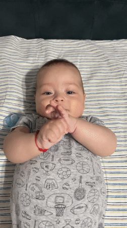 Baby on striped blanket, wide-eyed and thumb-curious