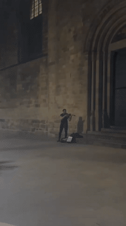 Street musician performs violin outside Barcelona stone building