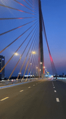Vehicle crosses illuminated cable-stayed bridge at dusk in Da Nang