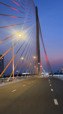 Vehicle crosses illuminated cable-stayed bridge at dusk in Da Nang